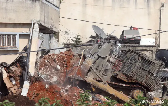 An Israeli military bulldozer smashes into the side of a home in the northwestern Israeli occupied West Bank town Qalqilya, during an Israeli incursion. The Israeli army entered the Palestinian town of Qalqilya surroundi...