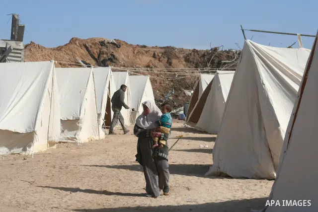A Palestinian woman carries her baby as she walks among tents erected to house those who lost their homes during the 22-day Israeli offensive in Jabalia in the northern Gaza Strip on January 31, 2009. A rocket fired by P...