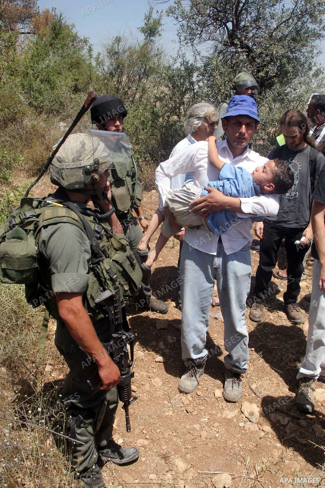 Israeli border police officers stand guard as a young Palestinian boy is evacuated down the mountainside after succumbing to tear-gas during a violent protest against the construction of Israel's controversial security f...