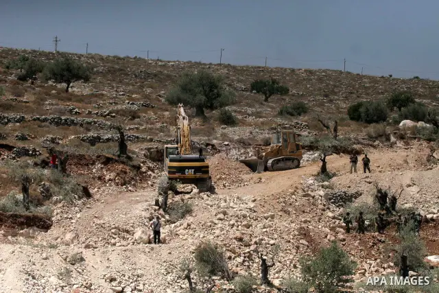 Israeli border police officers guard heavy machinery carving a route through Palestinian olive groves during a protest against the construction of Israel's controversial security fence in the West Bank village of Nilin,...