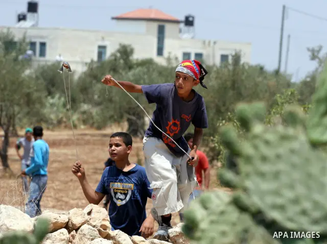 Palestinian boys hurl stones at Israeli border police officers during a demonstration against the construction of the controversial Israeli cement barrier in the West Bank village of Nilin near Ramallah. Sixteen Palestin...
