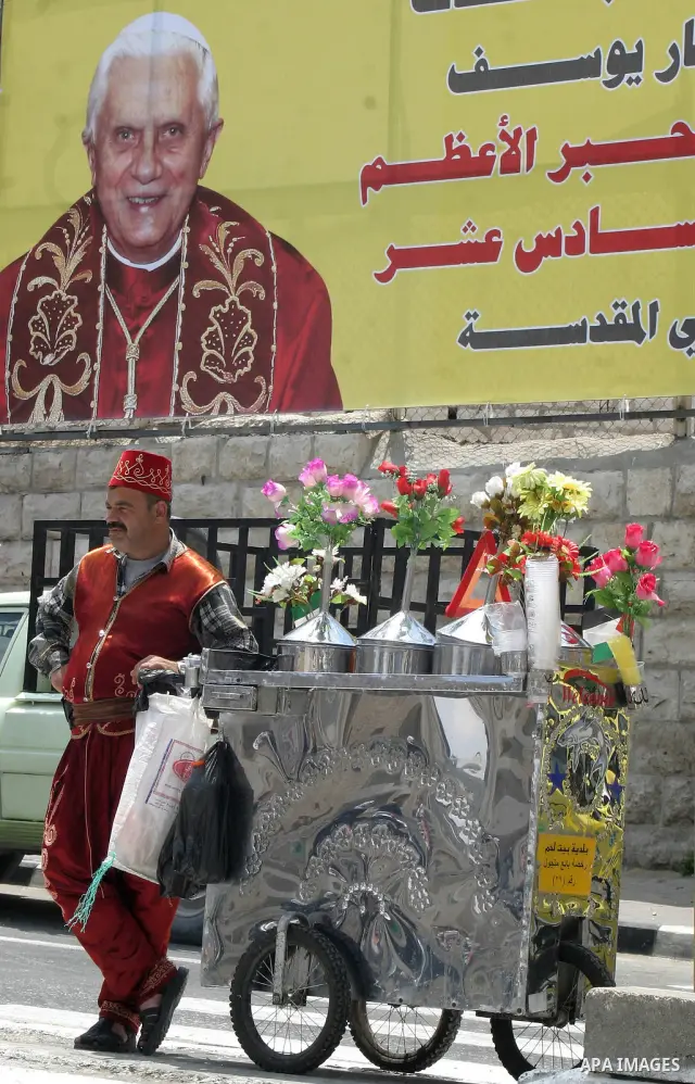 A drinks vendor serves customers next to a banner welcoming Pope Benedict XVI in the West Bank city of Bethlehem, on May 10, 2009, three days before the historic visit of the Pope. Pope Benedict XVI is on a week-long tou...