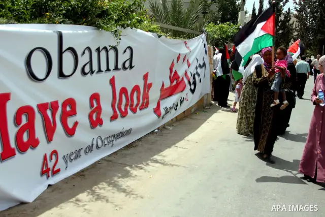 Palestinians holding his national flag walks past a banner that reads in Arabic and English "Obama have a look, 42 years of occupation" during a demonstration in the West Bank city of Bilin, near Ramallah, on June 4,2009...