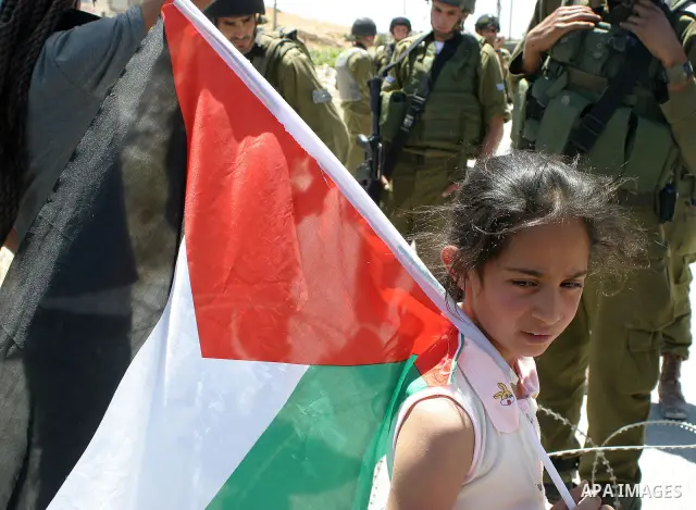 Israeli soldiers stand behind razor-wire and the Palestinian protesters girl hold Palestinian flag during a demonstration against the construction of Israel's separation barrier in the West Bank village of Maasarah near...