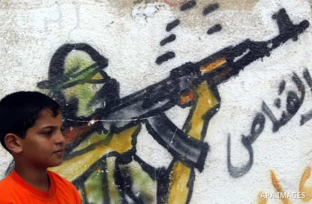 A Palestinian boys play ball next to a mural appear on it a Qassam Brigades Militants in Rafah refugee camp, southern Gaza Strip on 25 June 2009. Today marks the anniversary of the third year of the process of Qassam abd...