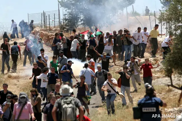 A Palestinian and foreign protestors run from a tear gas fired by Israeli soldiers during a demonstration against Israel's separation barrier in the West Bank village Bilin near Ramallah on July3, 2009. Photo by Nedal Sh...