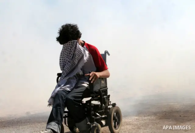 A foreign protestor in a wheelchair keep his face from a tear gas fired by Israeli soldiers during a demonstration against Israel's separation barrier in the West Bank village Bilin near Ramallah on July3, 2009. Photo by...