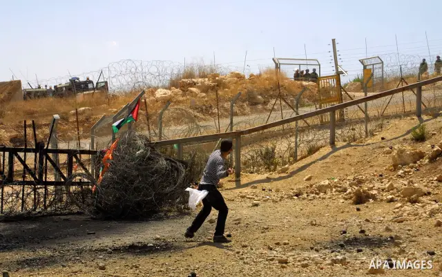 Palestinian youths throw stones at an Israeli soldiers during a protest against the construction of the West Bank separation barrier in the village of Nilin near Ramallah on Aug 7, 2009. Photo by Nedal Shtieh