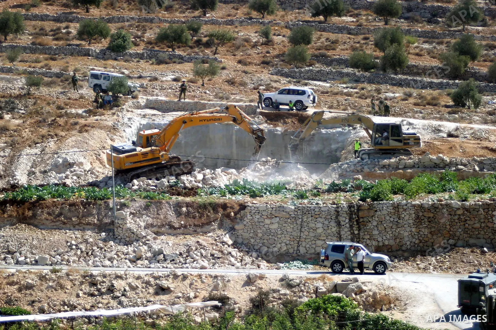 Israeli soldiers stand guard as a construction vehicle destroys a man-made reservoir on a Palestinian farm near the West Bank city of Hebron September 03, 2009. According to Israel's Civil Administration, the reservoir w...