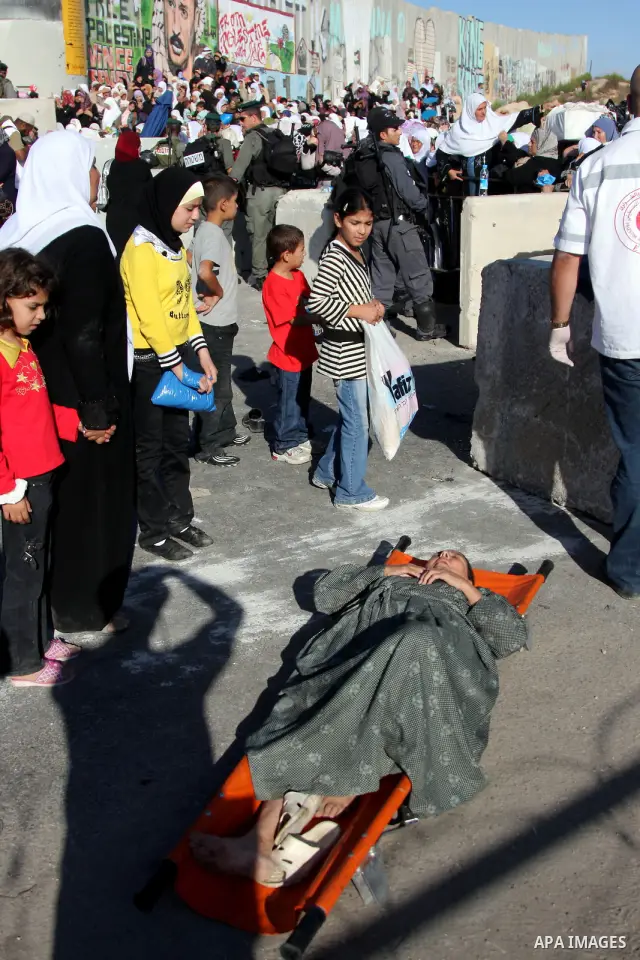 Palestinian woman is assisted after collapsing at the Israeli Kalandia checkpoint where she waited with other women to cross the checkpoint on their way to attend prayers in the Al-Aqsa Mosque compound in Jerusalem, on t...