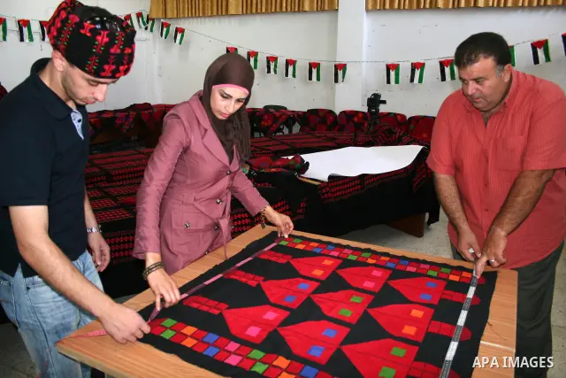 A Palestinian man and woman cut a piece of cloth with hand-knitted colourful motifs that will be used in making the largest traditional Palestinian dress in an attempt to enter the Guinness World Records in the West Bank...