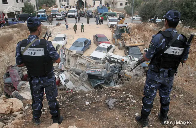 Palestinian policemen stand guard as a bulldozer destroys stolen cars during a continuing crackdown on stolen vehicles, illegally brought into the Palestinian territories in the West Bank town of Beit Fajjar near Bethleh...