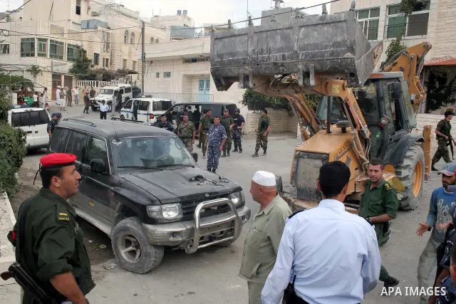 Palestinian policemen stand guard as a bulldozer destroys stolen cars during a continuing crackdown on stolen vehicles, illegally brought into the Palestinian territories in the West Bank town of Beit Fajjar near Bethleh...