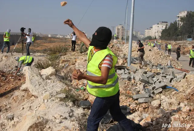 A Palestinian demonstrators throw stones at Israeli soldiers during a protest in the Qalandia refugee camp, near the West Bank city of Ramallah, on November 9, 2009 to mark the 20th anniversary of the fall of the Berlin...