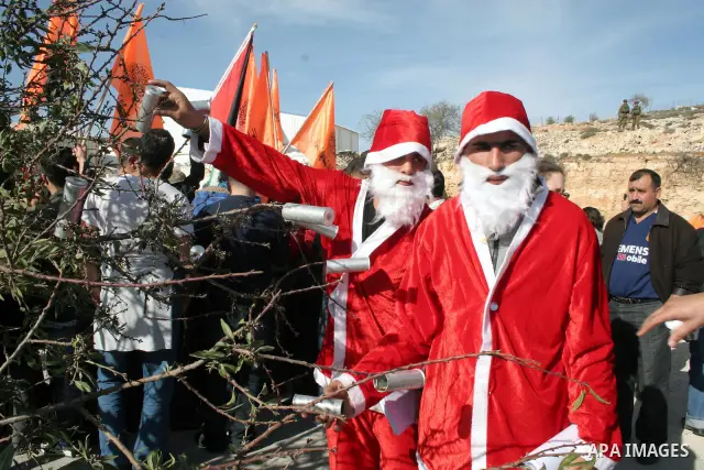 A demonstrator in a Santa Claus costume decorates a Christmas Tree with used Israeli army teargas canisters and sound bombs during a protest by Palestinians and foreign peace activists against Israel's controversial sepa...