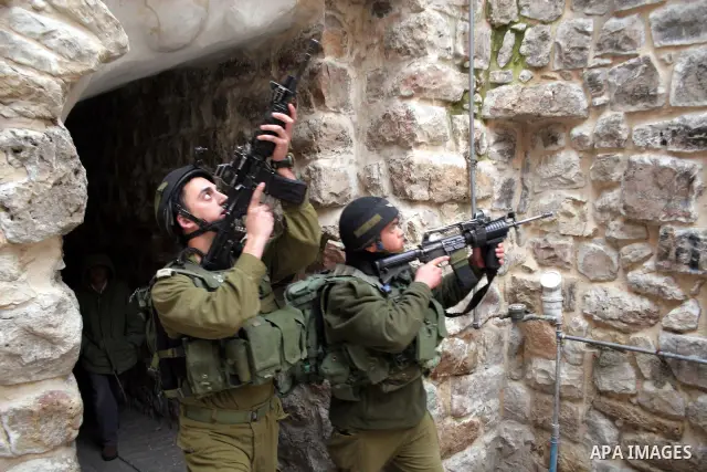 Israeli soldiers escort Jewish settlers as they walk past Palestinian shops during a tour in the old city of Hebron in the West Bank,January 30,2010. Photo by Najeh Hashlamoun