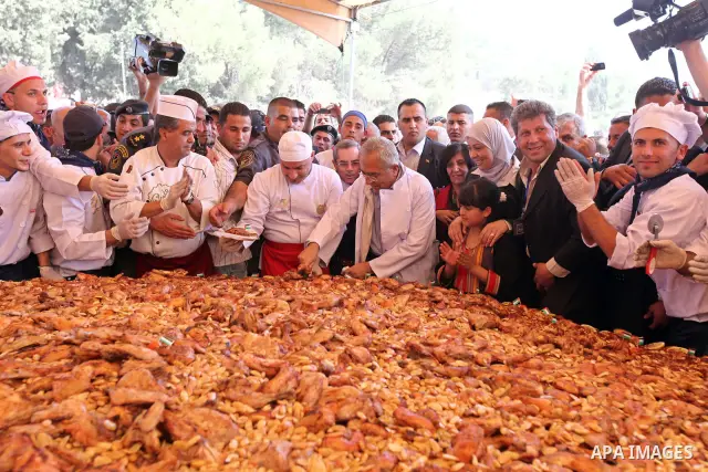 Palestinians Prime Minister Salam Fayyad (C) testing a massive dish of Musakhan, a traditional Palestinian food, in the West bank village of Arura, 19 April 2010. The dish has a diameter of 4 meters. Chefs are hoping to...