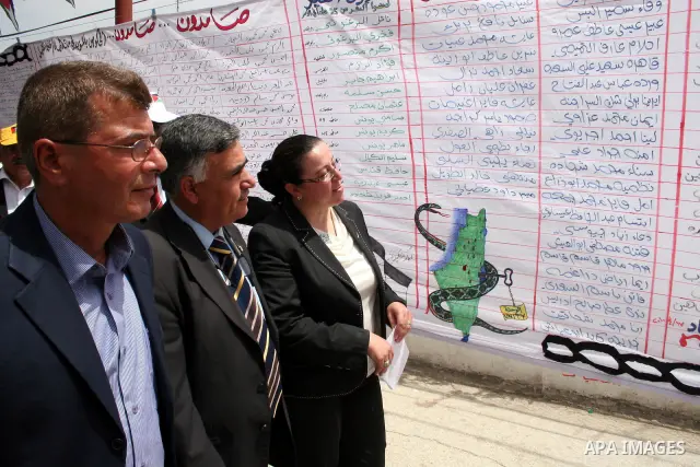 Minister prisoners Issa Qaraqe ( L ) Governor of Hebron Hussein Al-Aaraj ( C ) and the Director of Education Nasreen Ammer ( R ) walking past a banner bearing names of Palestinian prisoners held in Israeli jails during a...