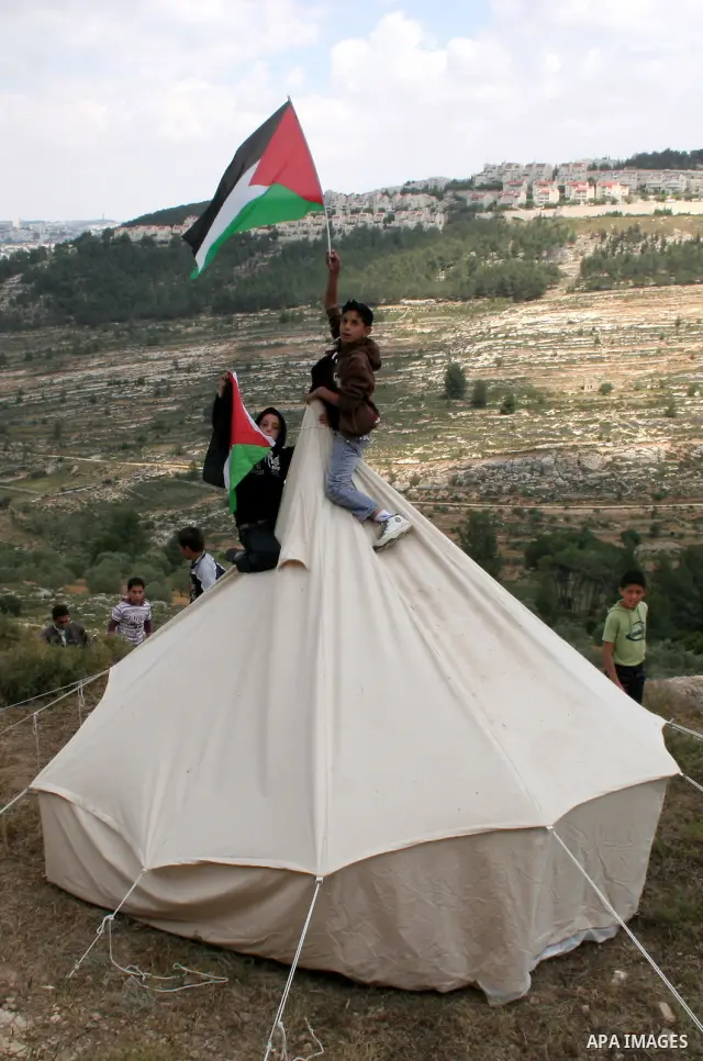 A Palestinian boy waves his national flag over a tent during a demonstration by Palestinians and foreign peace activists against Israel's controversial separation barrier in the West Bank village of Walajeh near the Pale...