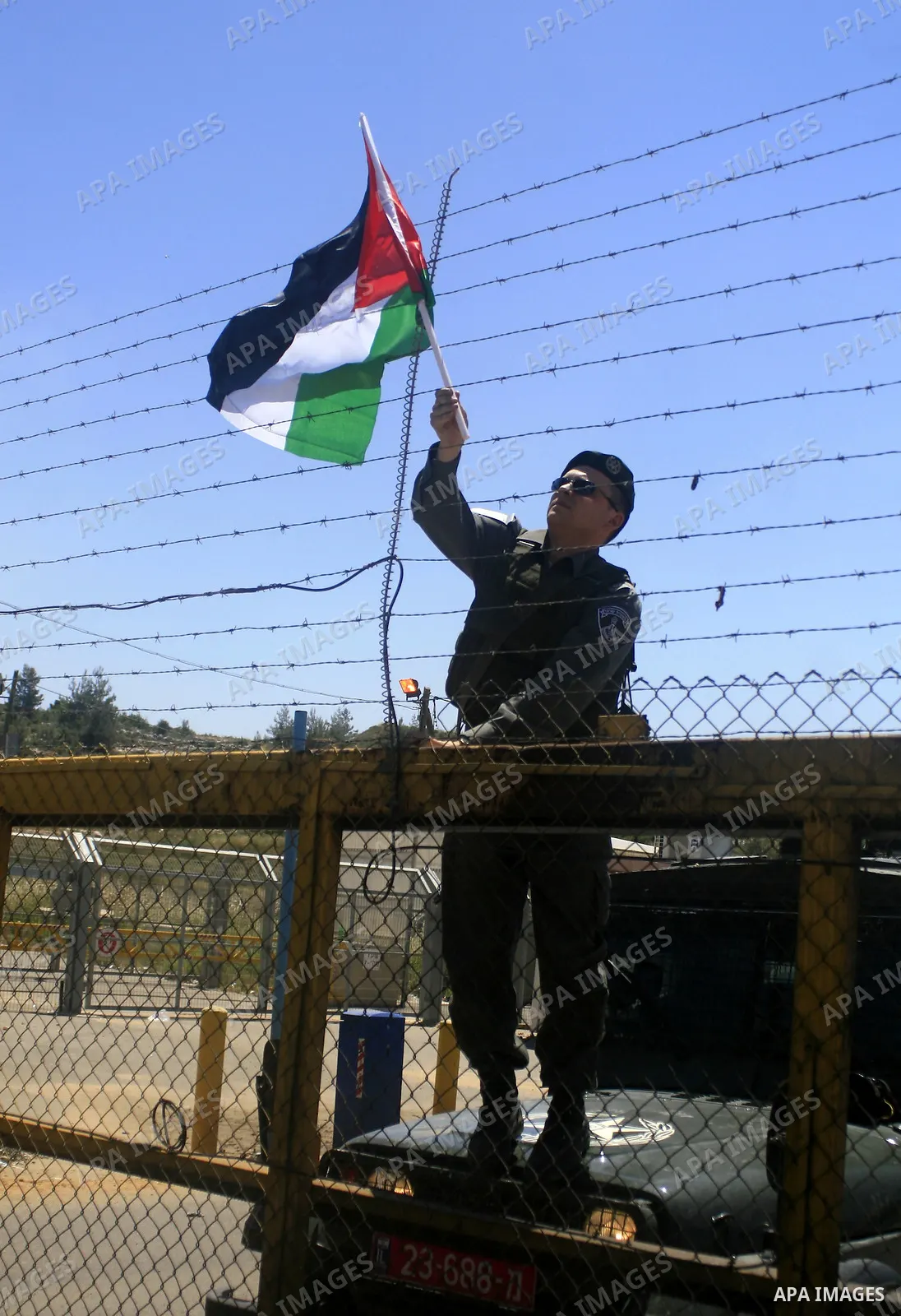 An Israeli border police officer takes down a Palestinian flag put up on a fence by a demonstrator during a protest outside Ofer prison near the West Bank city of Ramallah May 13, 2010, against the deportation by Israel...