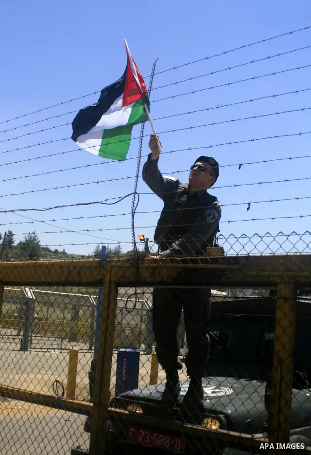 An Israeli border police officer takes down a Palestinian flag put up on a fence by a demonstrator during a protest outside Ofer prison near the West Bank city of Ramallah May 13, 2010, against the deportation by Israel...
