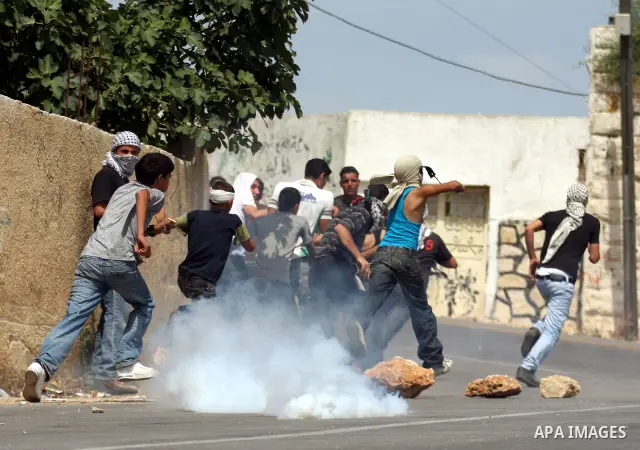 Palestinian youths run for cover from tear gas fired by Israeli troops during clashes following a demonstration in the West Bank village of Nabi Saleh on May 21, 2010 against the expansion of the nearby Jewish settlement...
