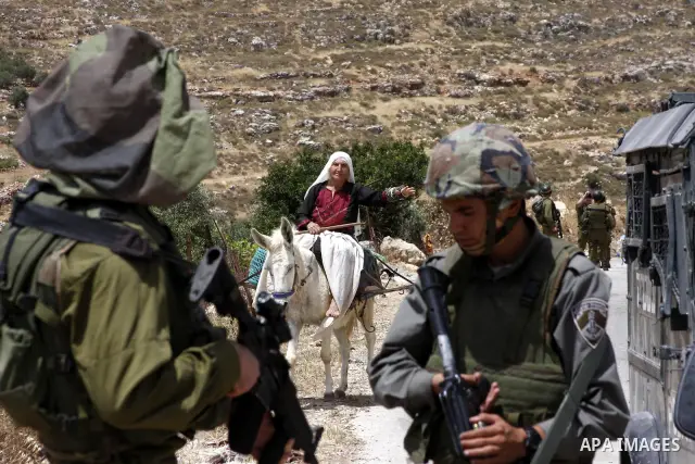 A Palestinian woman rides her donkey as she passes by Israeli soldiers guarding Israeli bulldozers which uproot olive trees to build the separation wall in the West Bank village of Nahalen, near Bethlehem, May 24, 2010....