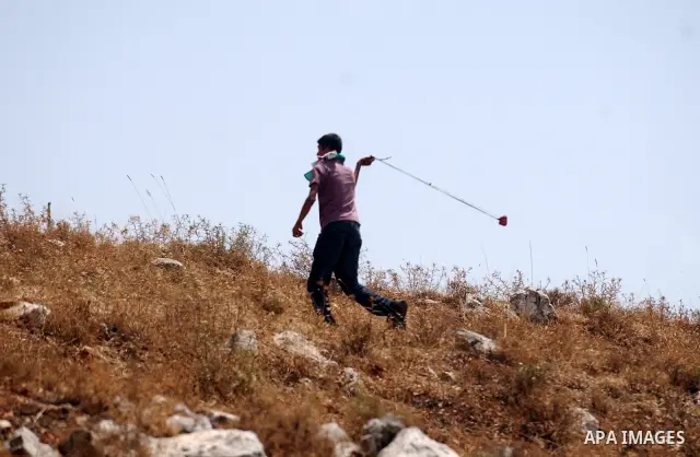 A Palestinian protester uses a sling to hurl stones at Israeli soldiers during clashes between demonstrators against the expansion of Jewish settlements in the occupeid West Bank and Israeli troops in the village of Iraq...