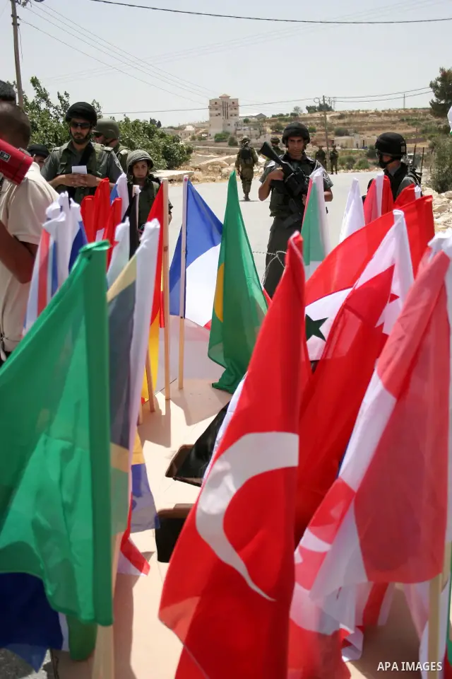 Israeli soldiers stand in front of Palestinian demonstrators holding up the Palestinian flag and various countries flags during a protest against Israel's separation barrier in the village of Maasarah, near the West Bank...