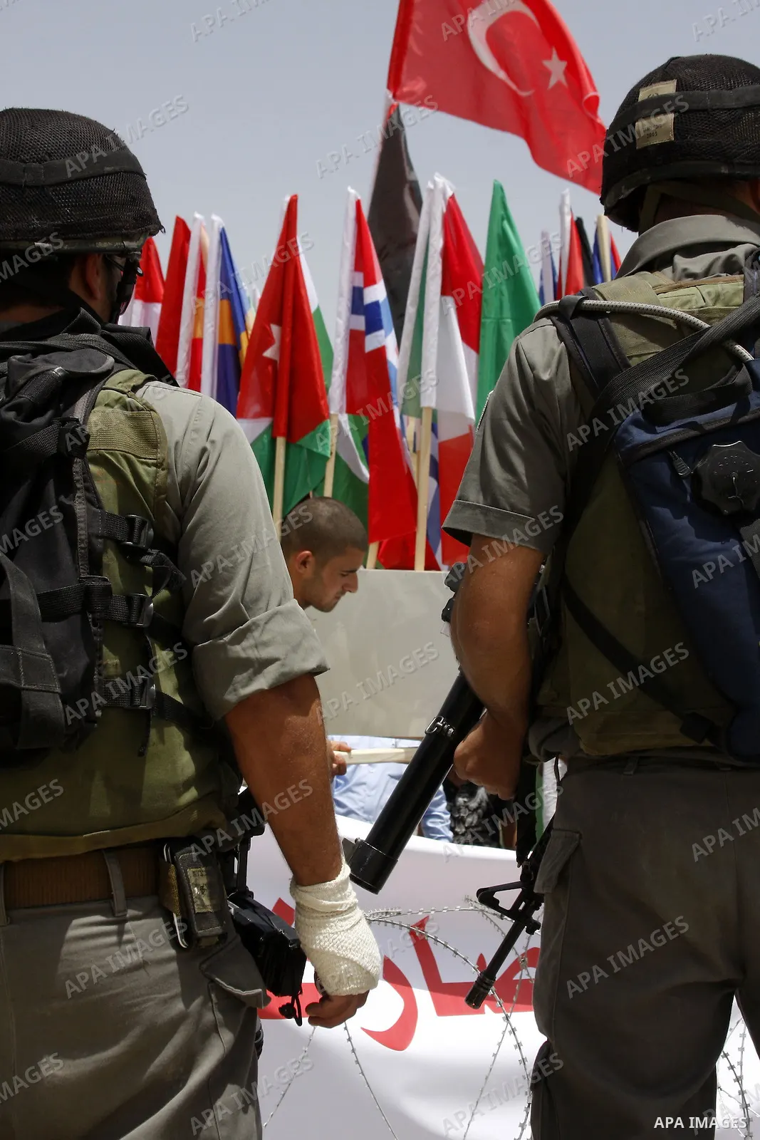 Israeli soldiers stand in front of Palestinian demonstrators holding up the Palestinian flag and various countries flags during a protest against Israel's separation barrier in the village of Maasarah, near the West Bank...