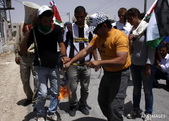 A Palestinian protester burns the Israeli flag during a demonstration by Palestinian, Israeli and foreign peace activists against Israel's controversial separation barrier in the West Bank village of Maasarah, near the b...