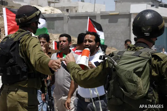 Israeli soldiers stand in front of Palestinian demonstrators holding up the Palestinian flag during a protest against Israel's separation barrier in the village of Maasarah, near the West Bank city of Bethlehem, on June...