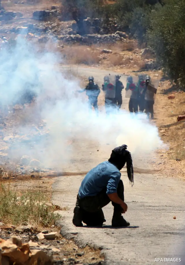 Palestinian protester takes cover from tear gas canisters fired by Israeli soldiers during a demonstration against Israel's separation barrier in the West Bank village of Bilin near Ramallah, Friday, July 2, 2010. Israel...