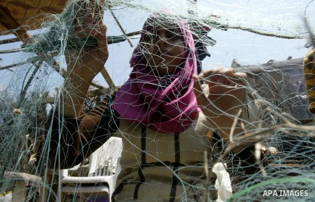 Madlin, her brother Kayed and sister Reem fix their fishing net at a hut on the beach of Gaza City on July 25, 2010. Madlin is the first girl in the Gaza Strip to fish professionally in order to support her poor family....