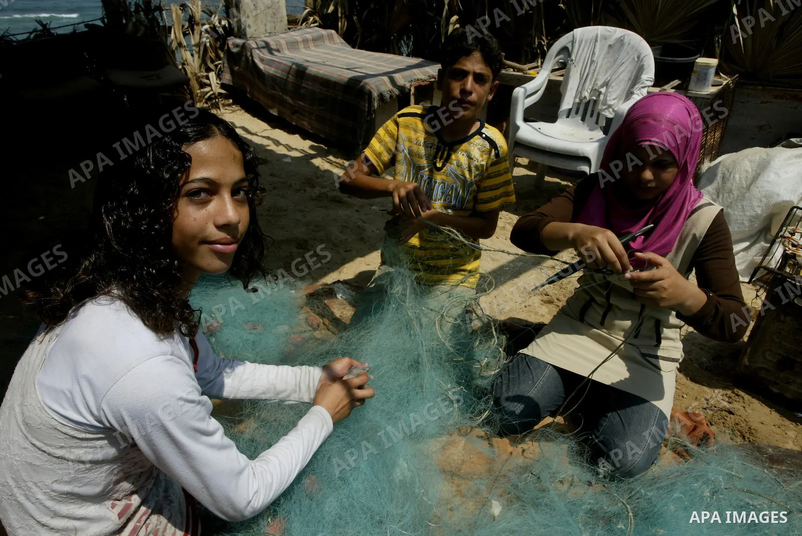 Madlin, her brother Kayed and sister Reem fix their fishing net at a hut on the beach of Gaza City on July 25, 2010. Madlin is the first girl in the Gaza Strip to fish professionally in order to support her poor family....