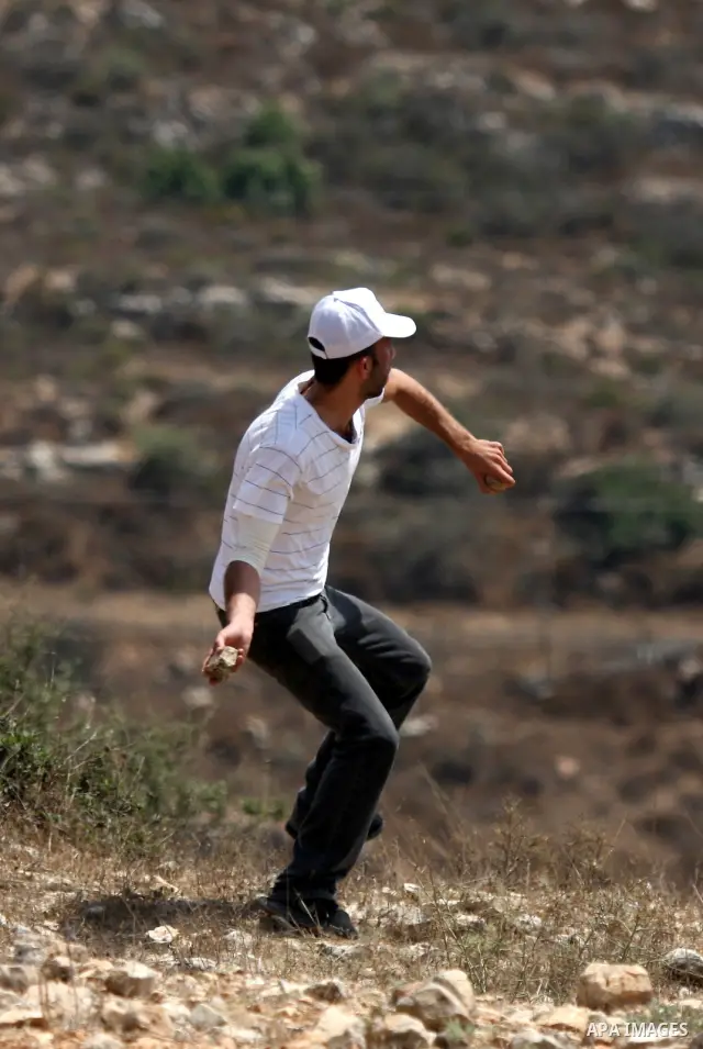 A Palestinian protester throws stones at Israeli troops, during a demonstration by Palestinian, Israeli and international activists against the expansion of the nearby Jewish settlement of Halamish in the West Bank villa...