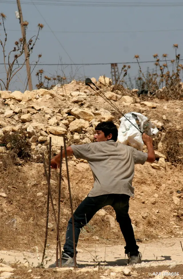 A Palestinian boy uses slingshot to throw stones at Israeli soldiers during a demonstration against Israeli settlements, in the West Bank village of Beit Omar, near Hebron, Saturday, on August 7, 2010.. Photo by Mamoun W...