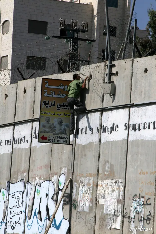 A Palestinian man climbs a ladder to cross Israel's separation barrier on his way to attend prayers in the Al-Aqsa Mosque compound in Jerusalem, in the West Bank town of Al-Ram, just outside Jerusalem, Friday Aug. 13, 20...
