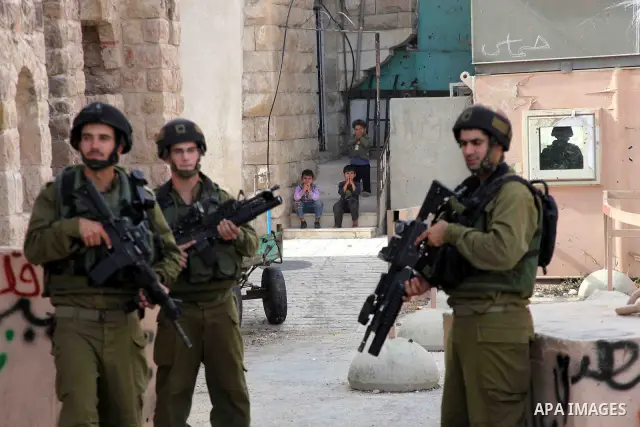 Israeli soldiers stand guard as Palestinian boys hurl stones towards Israeli troops during clashes with Palestinian stone-throwers in the West Bank city of Hebron on October 10, 2010. Photo by Najeh Hashlamoun