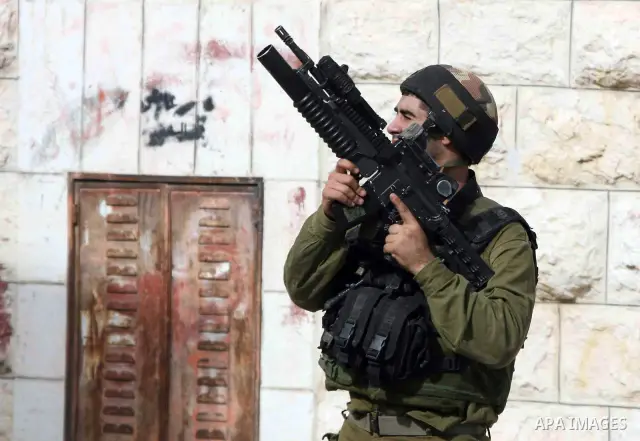 An Israeli soldier stands guard as Palestinian boys hurl stones towards Israeli troops during clashes with Palestinian stone-throwers in the West Bank city of Hebron on October 10, 2010. Photo by Najeh Hashlamoun