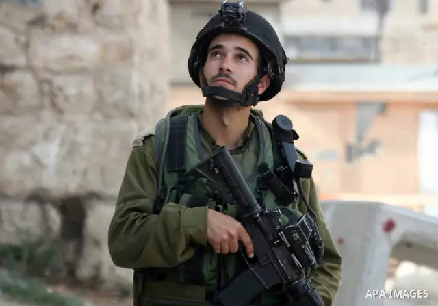 An Israeli soldier stands guard as Palestinian boys hurl stones towards Israeli troops during clashes with Palestinian stone-throwers in the West Bank city of Hebron on October 10, 2010. Photo by Najeh Hashlamoun