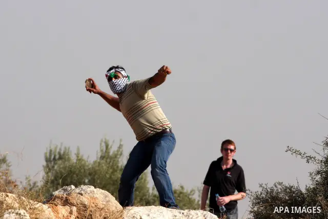 A Palestinian youth hurls stones towards Israeli soldiers during a protest against Israel's separation barrier as masked Palestinian stones throwers clash with Israeli soldiers in the West Bank village of Bilin, near Ram...