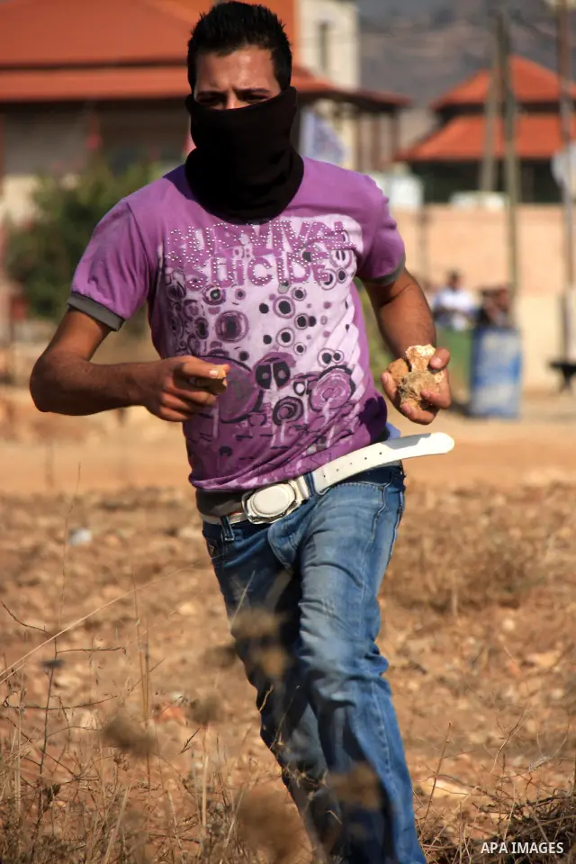 A Palestinian youth hurls stones towards Israeli soldiers during a protest against Israel's separation barrier as masked Palestinian stones throwers clash with Israeli soldiers in the West Bank village of Bilin, near Ram...