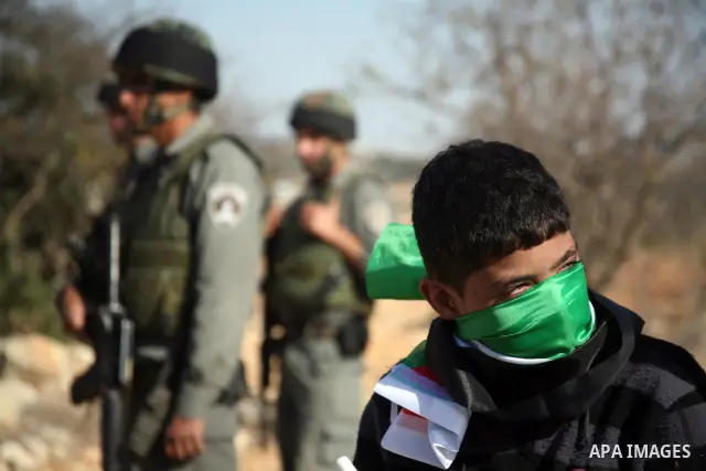 Israeli soldiers stand guard as Palestinian boy cover his face with national flag during a demonstration by Palestinian, Israeli and foreign activists against the demolishing of farm land to be used in the construction o...