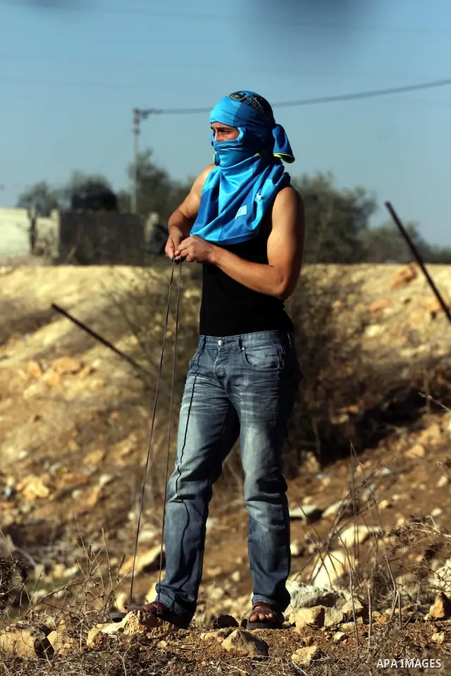 A Palestinian protester uses a sling to hurl stones towards Israeli border police in the West Bank village of Nabi Saleh near Ramallah, during a demonstration against the expropriation of Palestinian land to expand the n...