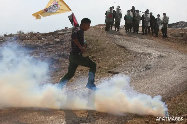 Palestinian protesters run for cover from tear gas thrown by Israeli soldiers during a protest against the construction of the Israeli controversial separation barrier in the West Bank village of Bilin near Ramallah on,...