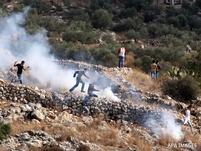 Palestinian protesters run for cover from tear gas thrown by Israeli soldiers during a protest against the construction of the Israeli controversial separation barrier in the West Bank village of Bilin near Ramallah on,...