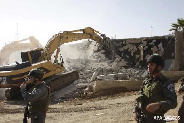 Israeli soldiers stand guard as bulldozers demolish a Palestinian building in the occupied West Bank city of Hebron on December 20, 2010. Photo by Najeh Hashlamoun