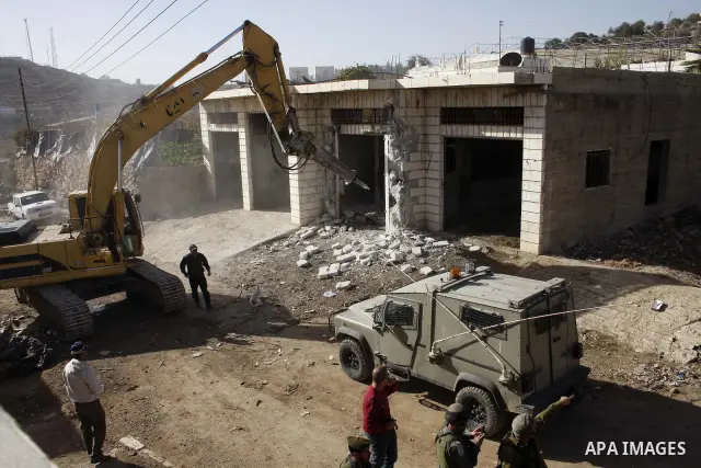 Israeli soldiers stand guard as bulldozers demolish a Palestinian building in the occupied West Bank city of Hebron on December 20, 2010. Photo by Najeh Hashlamoun