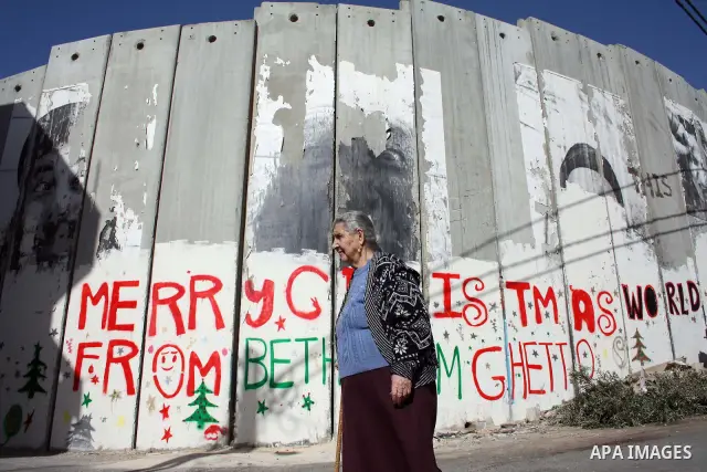 Palestinian christian woman walks past Christmas graffiti painted on the Israeli separation barrier in the West Bank town of Bethlehem, as Christmas approaches, on December 22, 2010. Photo by Najeh Hashlamoun